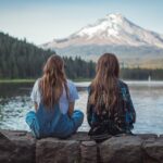 Two women sitting by a lake with a stunning view of Mount Hood in Oregon during sunset.