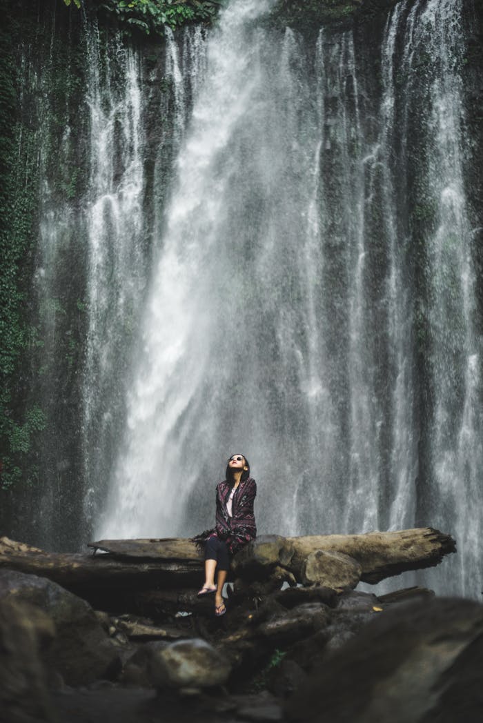 A serene scene featuring a woman at a waterfall in West Nusa Tenggara, Indonesia.